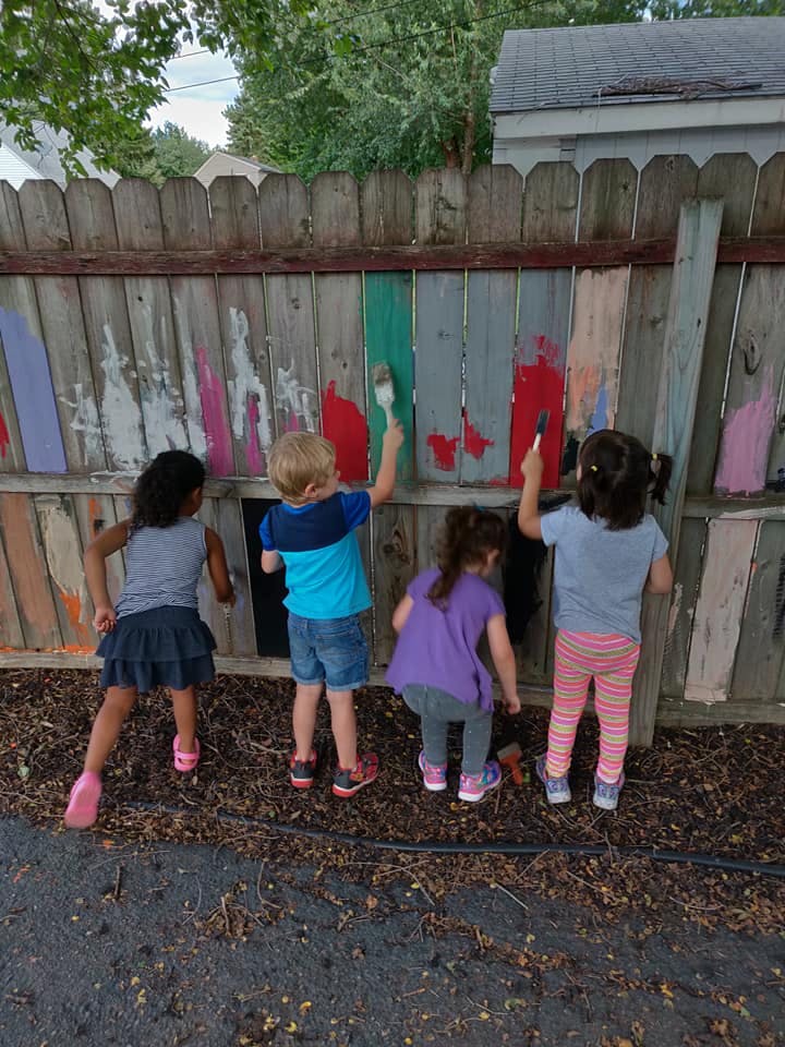 Four children painting a wooden fence outdoors