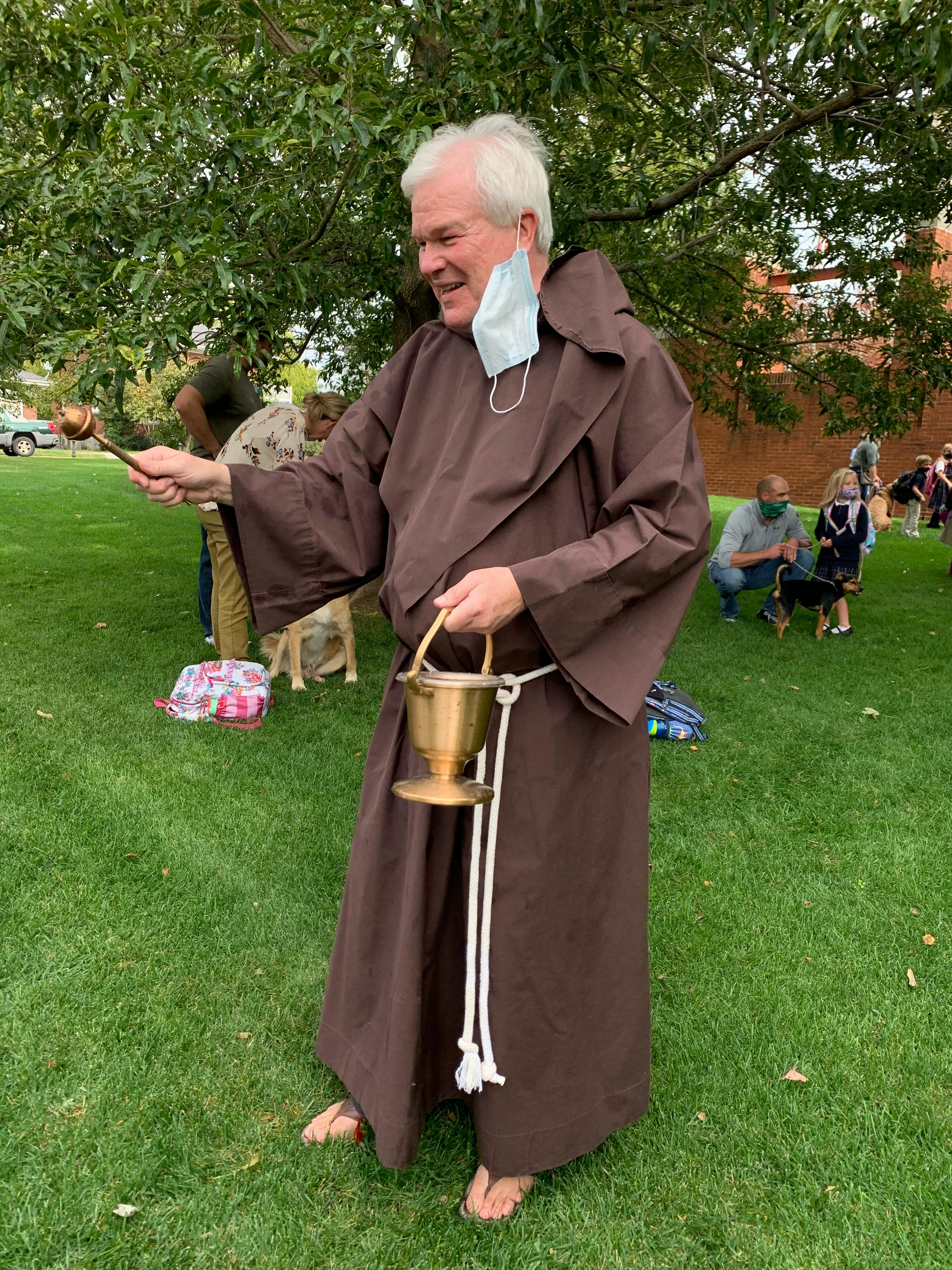 Person in a brown robe holding a sprinkler and a brass bucket