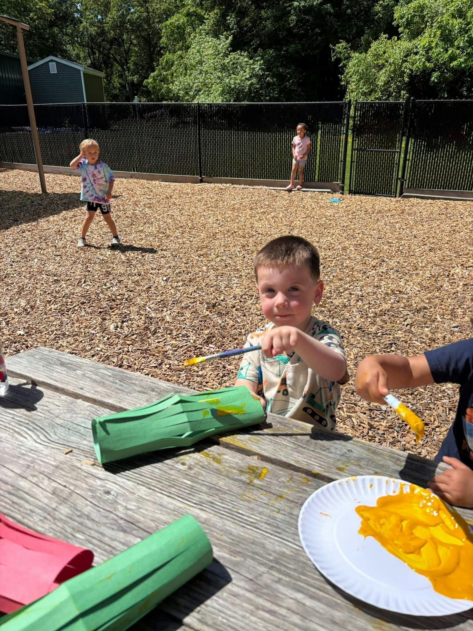 Child painting a green paper lantern at a picnic table