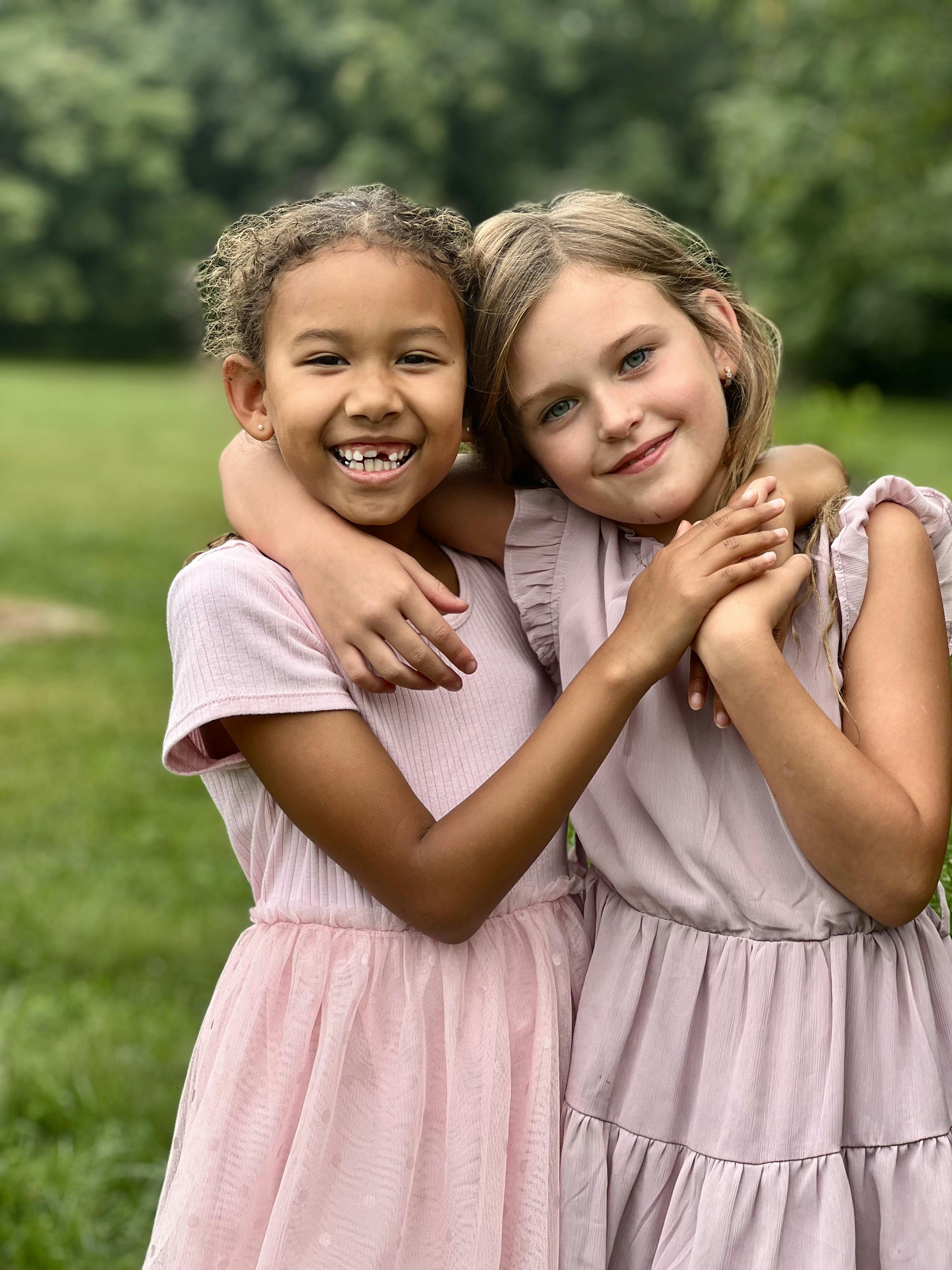 Two children in matching dresses hugging outdoors