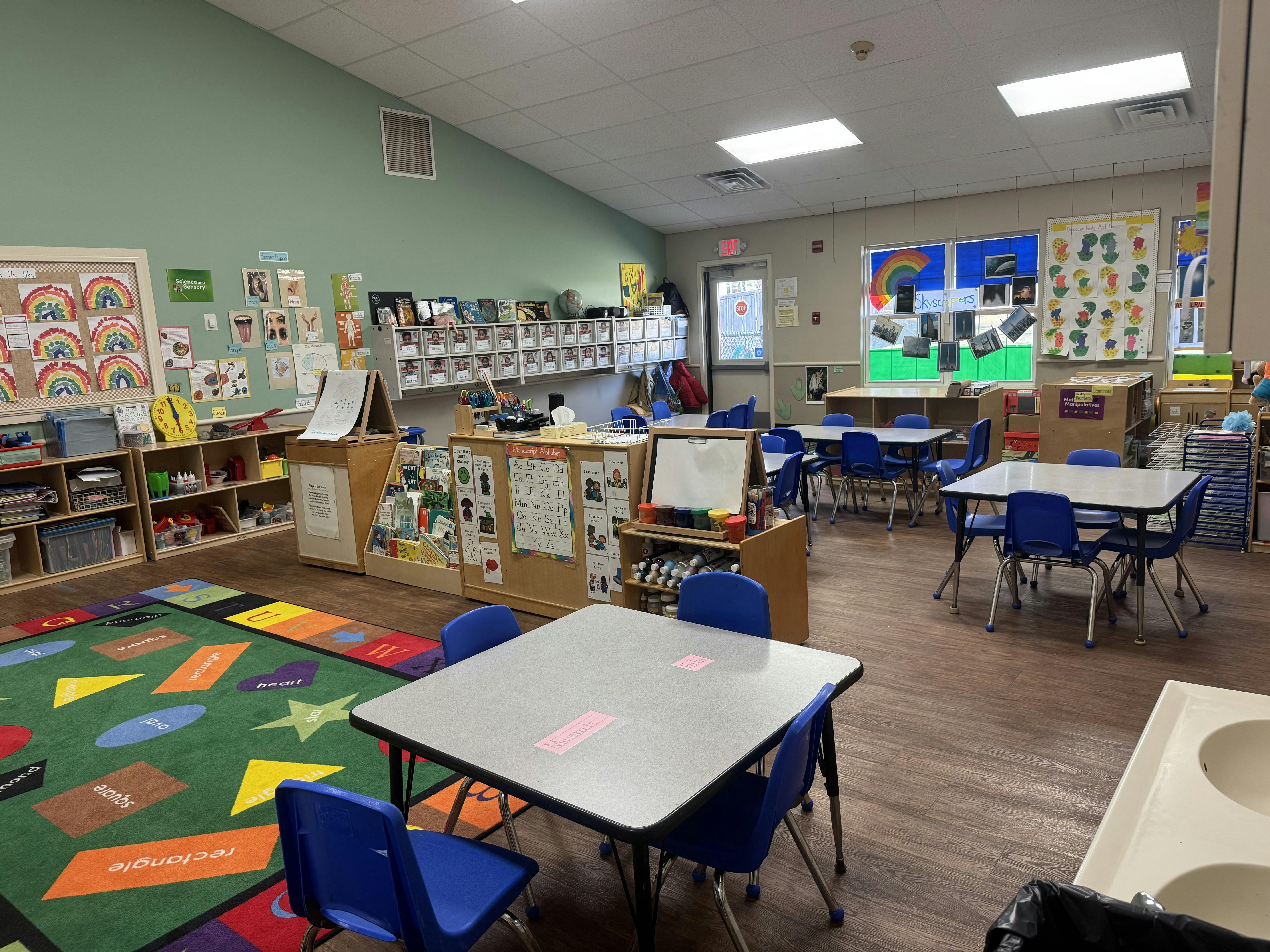 Classroom with small tables and chairs, an alphabet rug, and colorful decorations