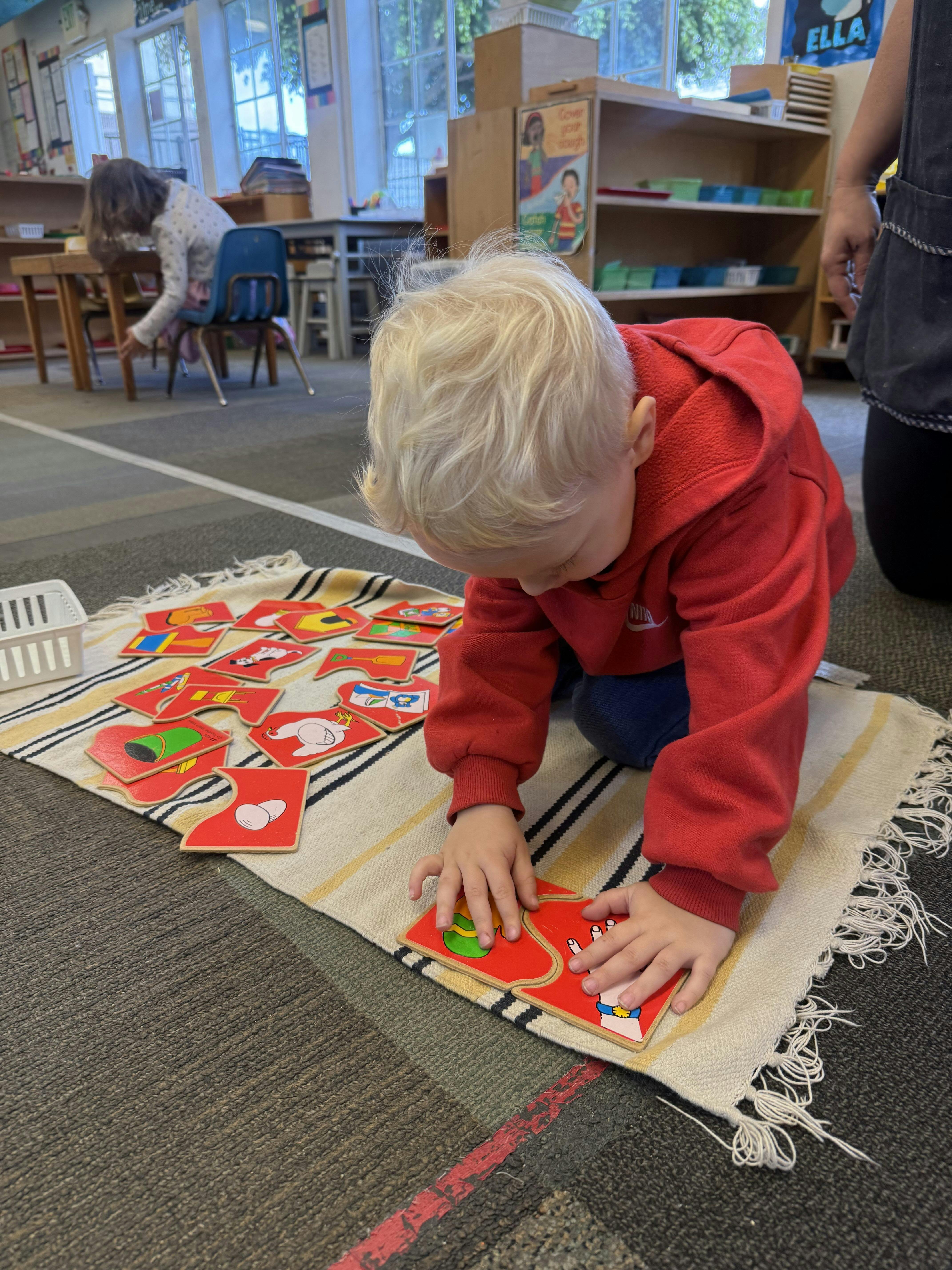 Child kneeling on a mat and assembling puzzle pieces in a classroom