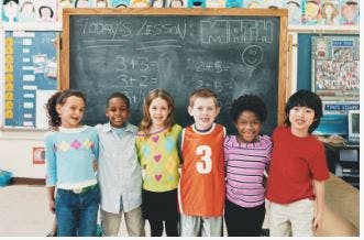 Six children standing in front of a chalkboard in a classroom
