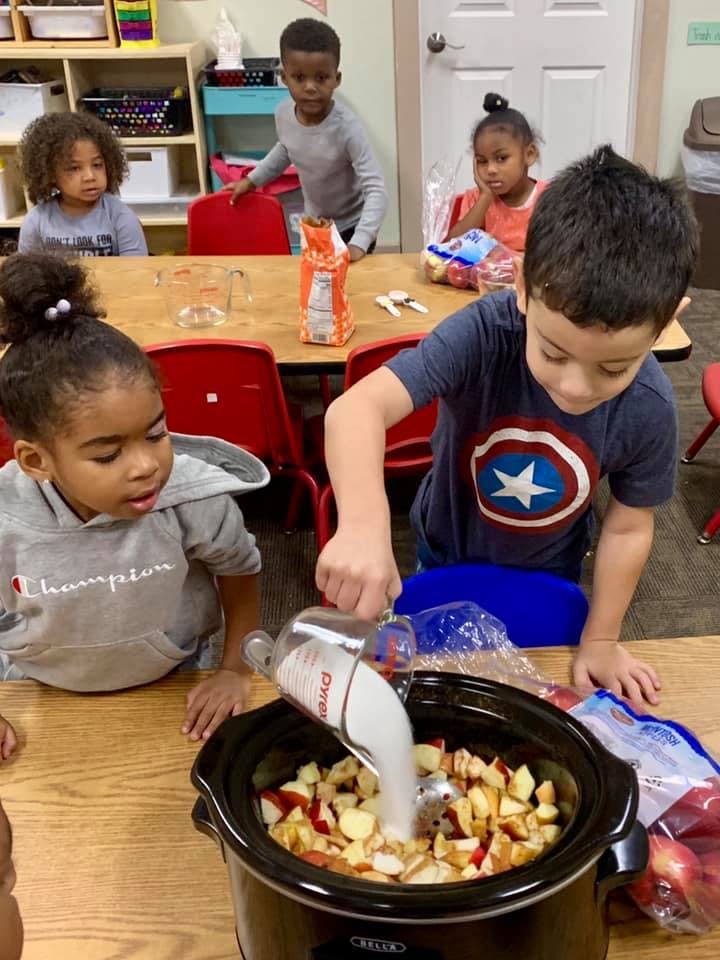 Child pouring liquid into a slow cooker with chopped apples