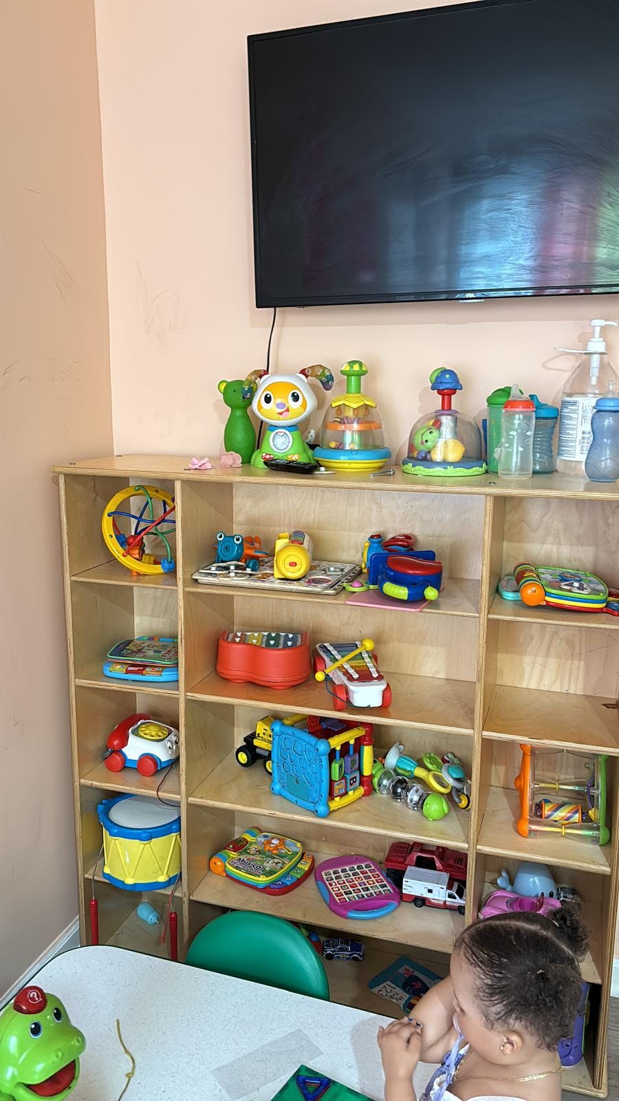 Child at a table next to shelves filled with children's toys and a television