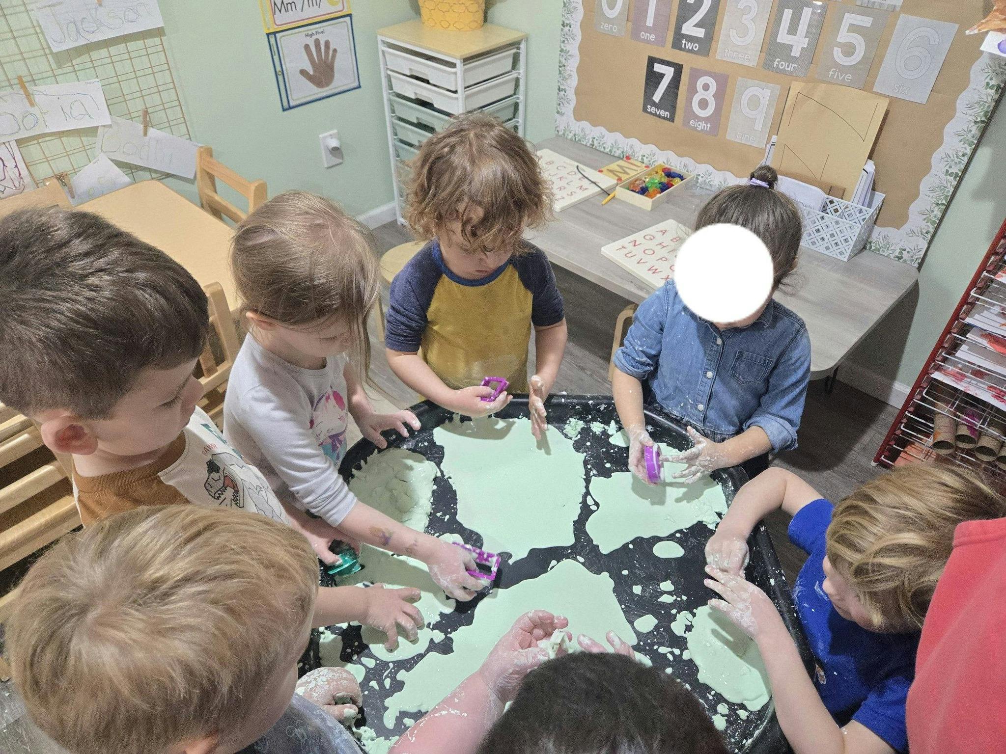 Children playing with a green substance in a black tray in a classroom
