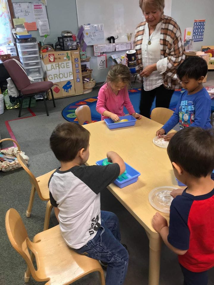 Adult supervising children playing with sensory bins at a table
