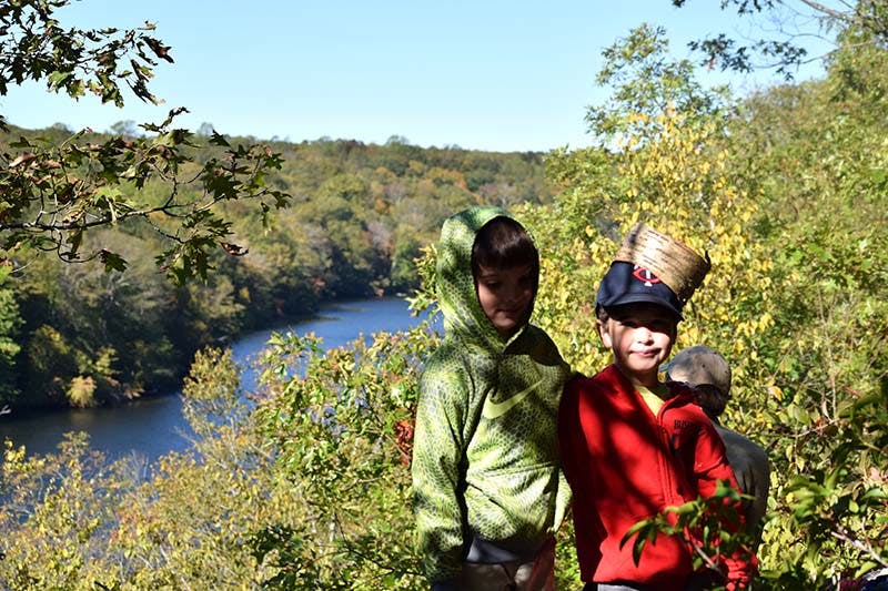 Three children standing in front of a river and trees