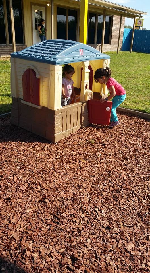 Two children playing in a plastic playhouse on wood chips