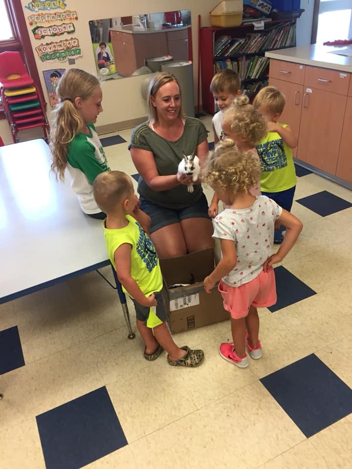Adult holding a small animal surrounded by children in a classroom