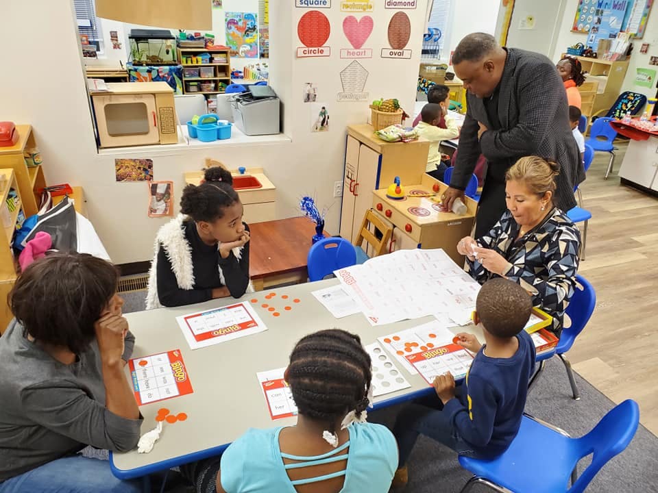 Adults and children sitting at a table with papers and small objects