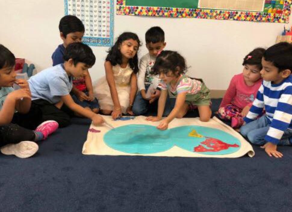 Children sitting on the floor around a mat with a map