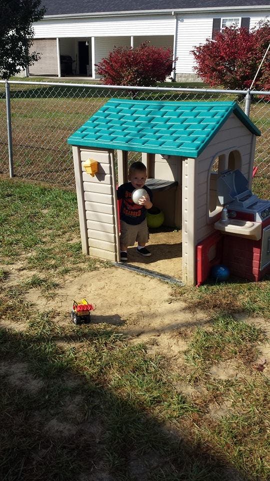 Child standing in a playhouse holding a ball
