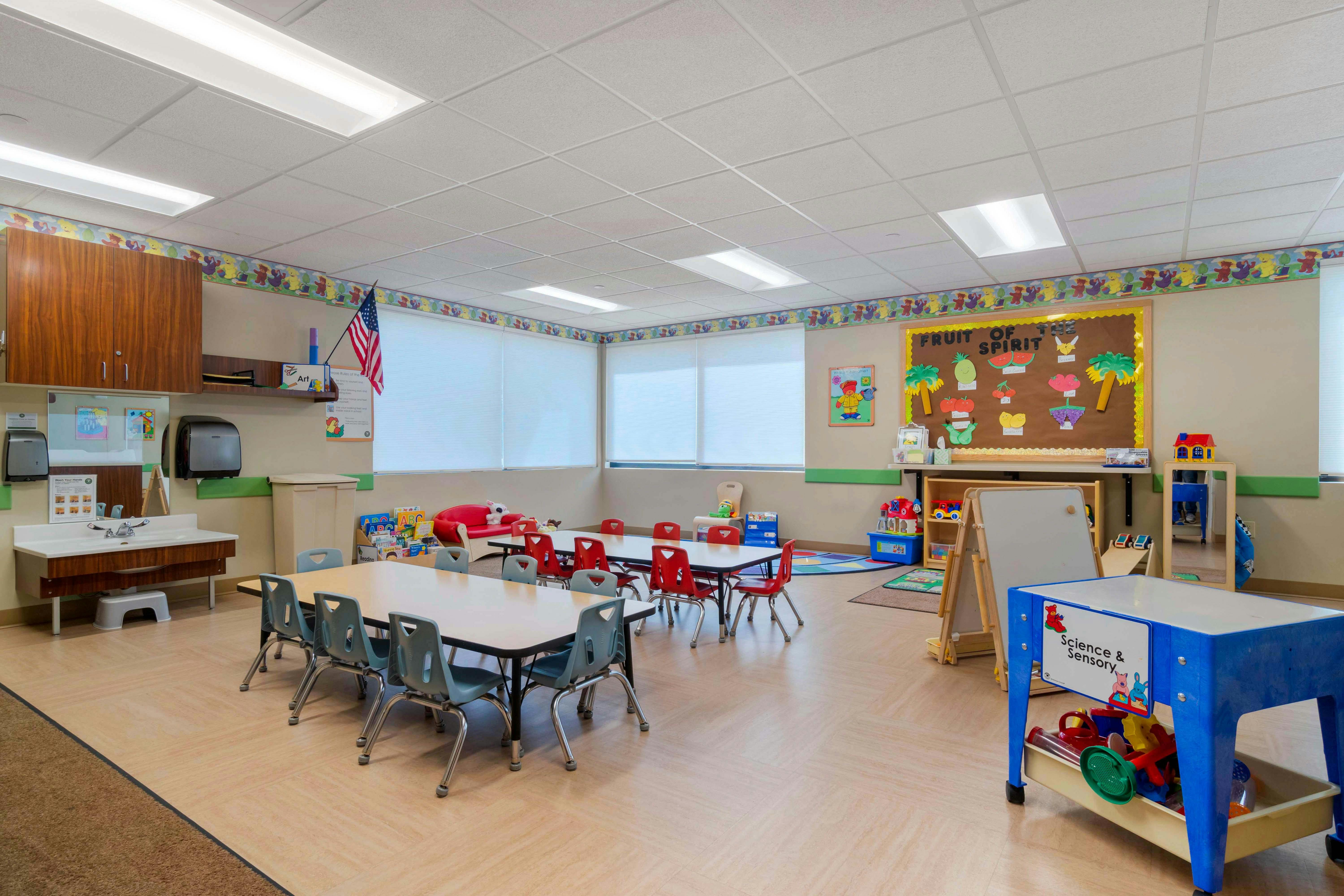 Classroom with child-sized tables and chairs, a sink, and a bulletin board