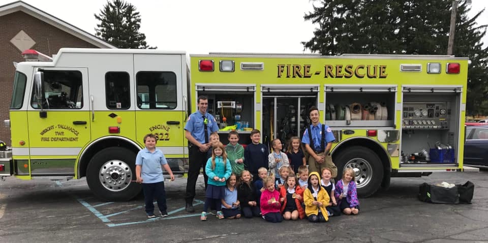 Two people and a group of children posing in front of a fire truck