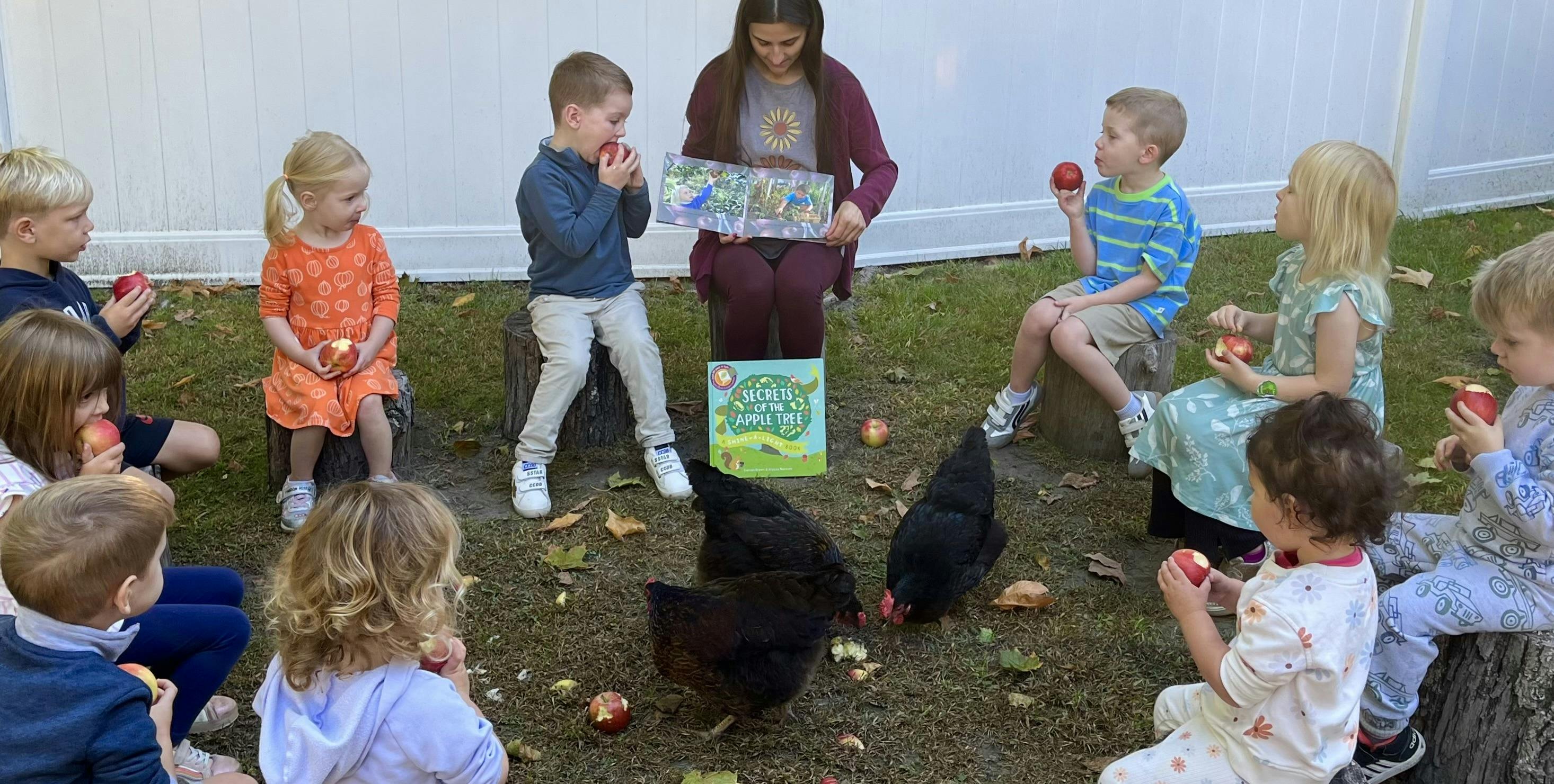 People reading and eating apples outdoors with chickens nearby