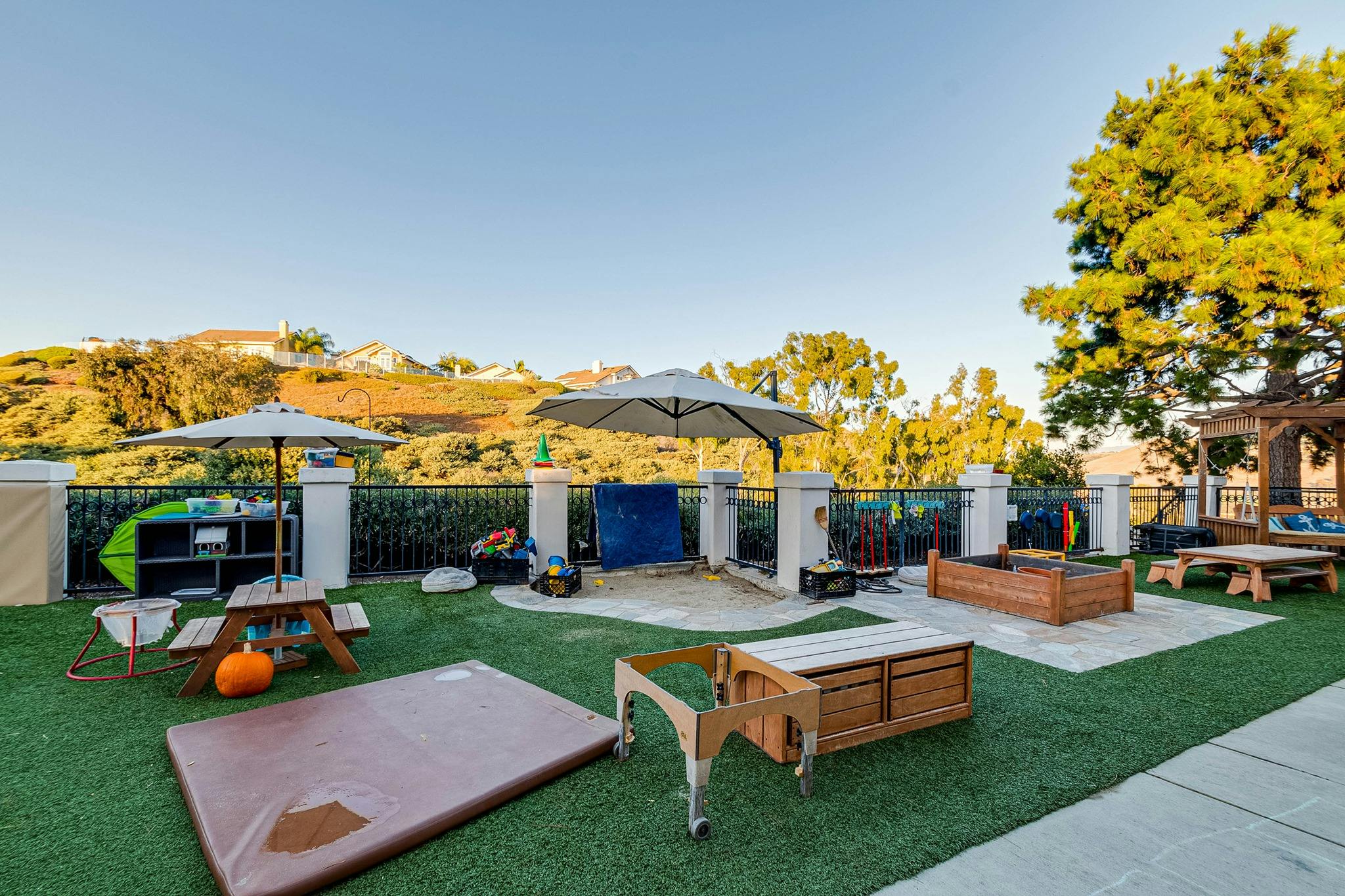 Outdoor play area with artificial turf, umbrellas, and various play equipment