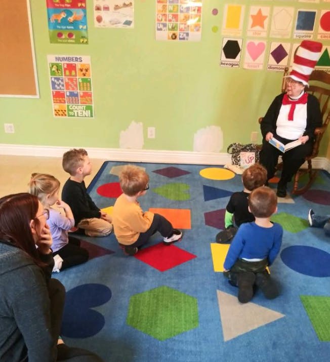 Person in striped hat reading to children in a classroom