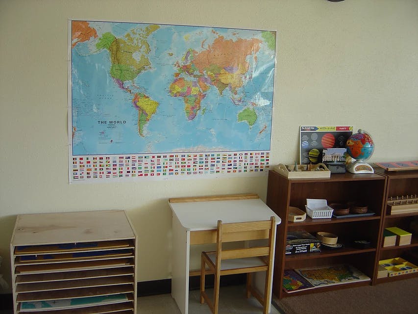 World map on a wall above a small desk and shelves with shelves