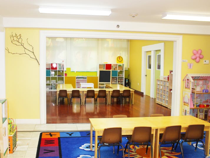 Classroom with tables and chairs, colorful rug, and shelves