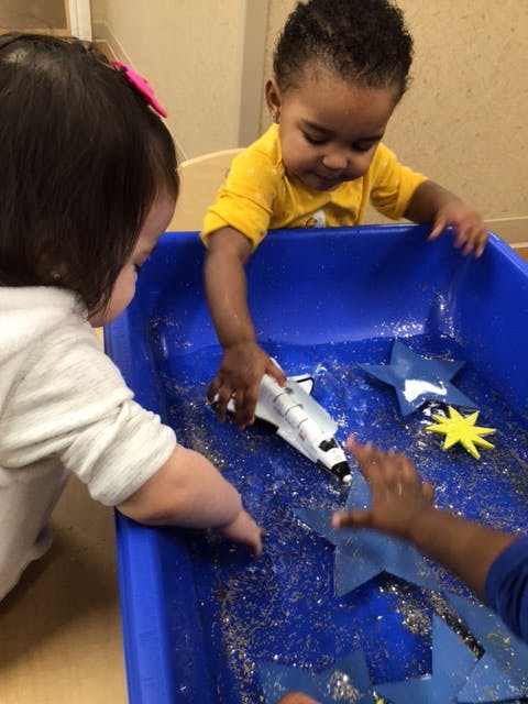 Two children playing with a toy space shuttle and stars in a blue bin