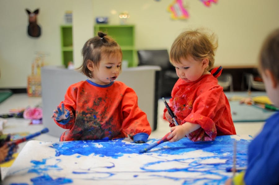Two children painting with blue paint in a classroom