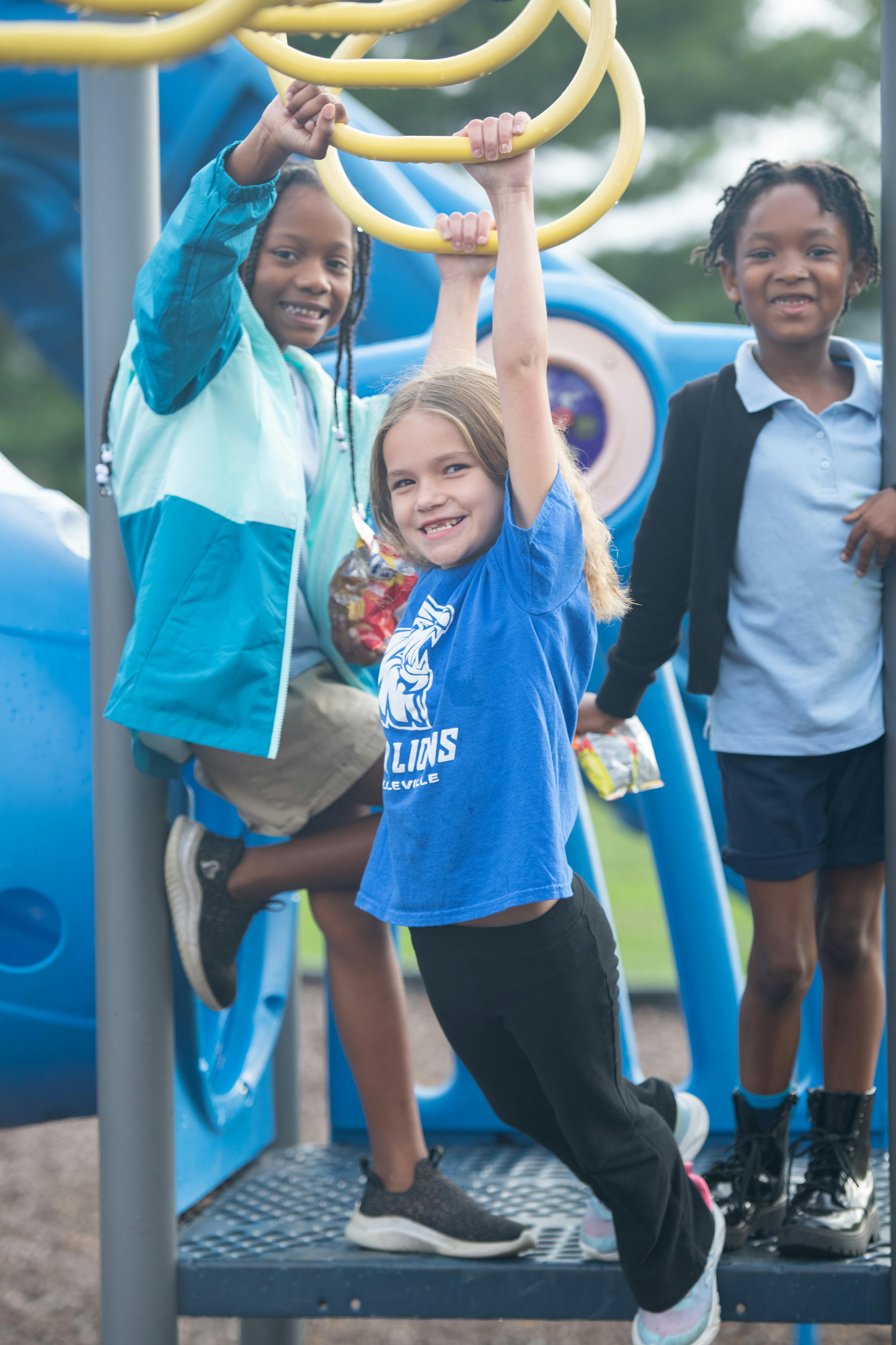 Three children playing on monkey bars on a blue playground structure
