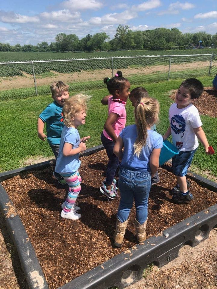 Group of children playing in a raised garden bed filled with wood chips