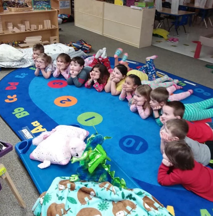 Children lying on their stomachs on a blue rug in a classroom
