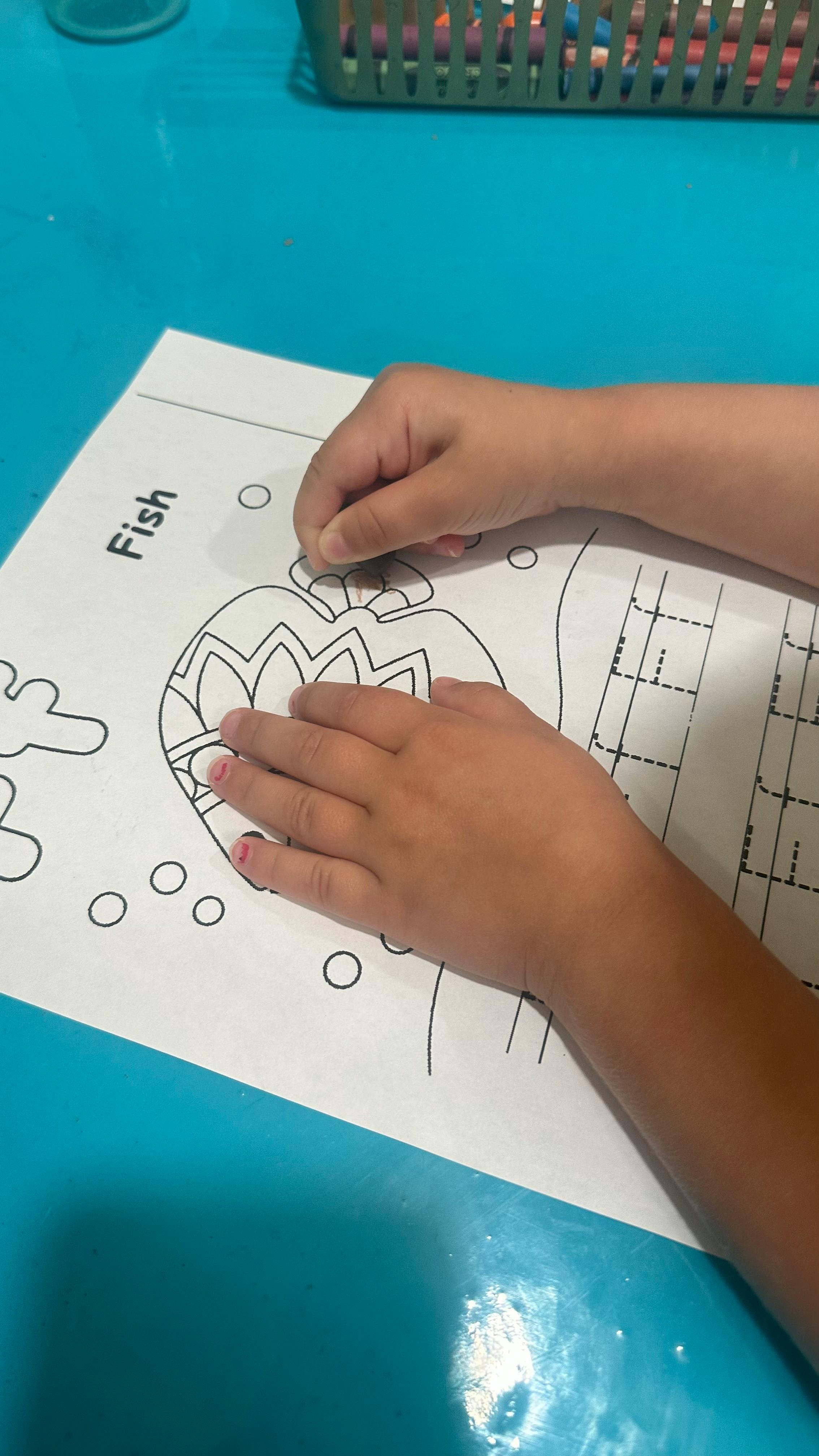 Child's hands coloring a fish outline on a paper