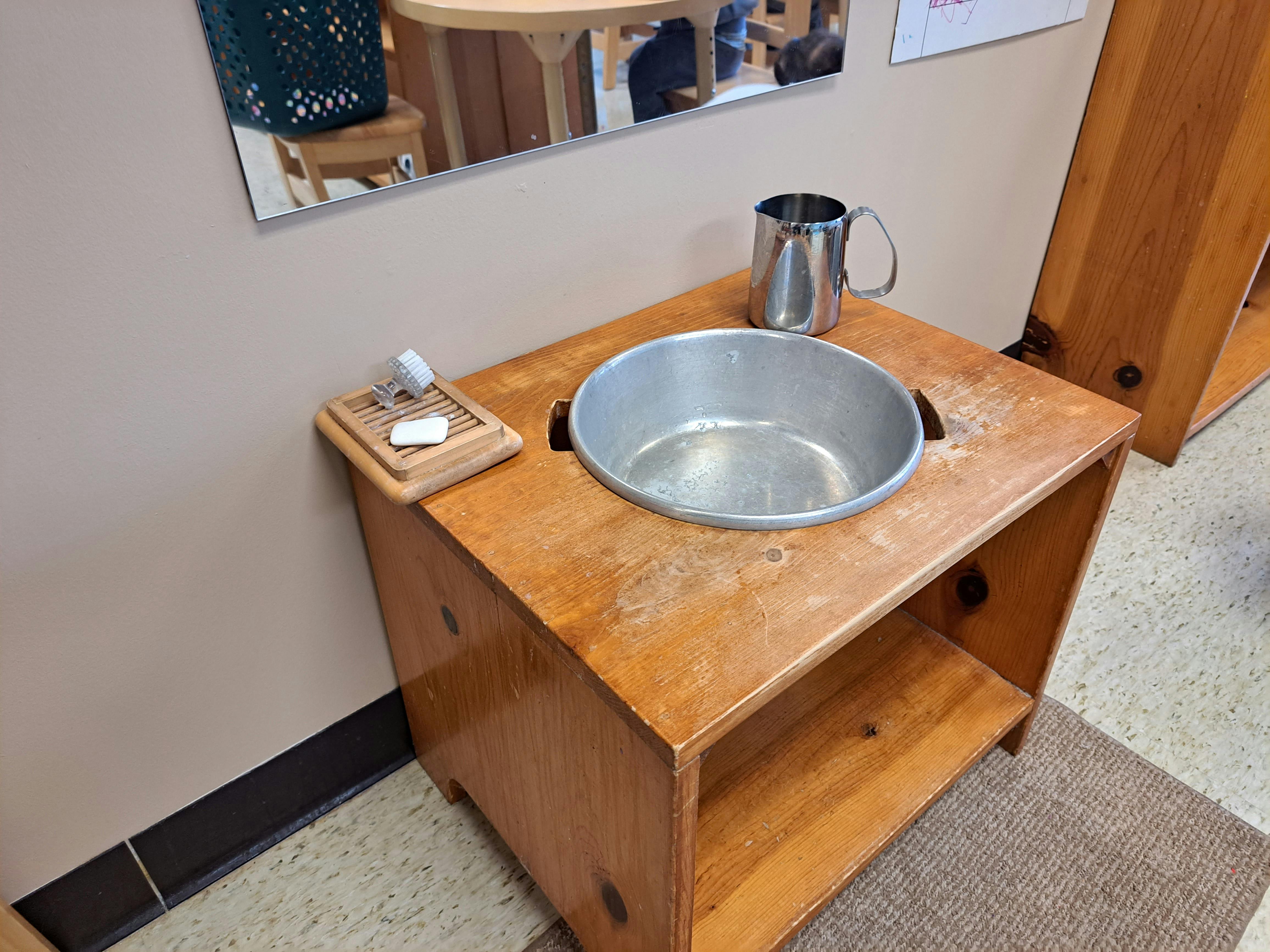 Wooden washstand with a metal basin, soap, and a metal cup
