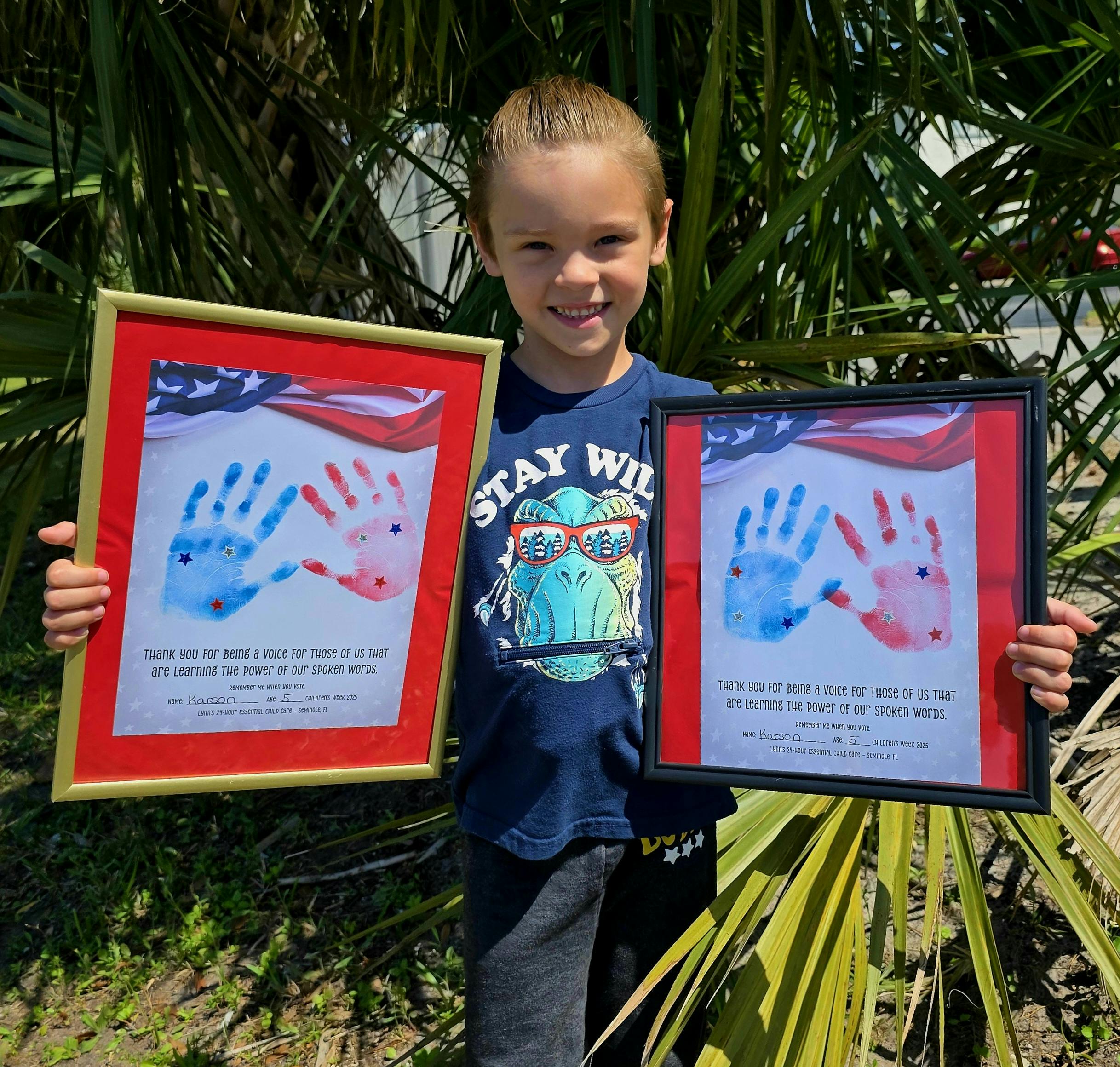 Child holding two framed pictures of handprints
