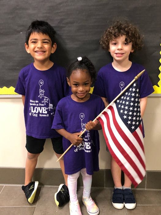 Three children in purple shirts, one holding an American flag