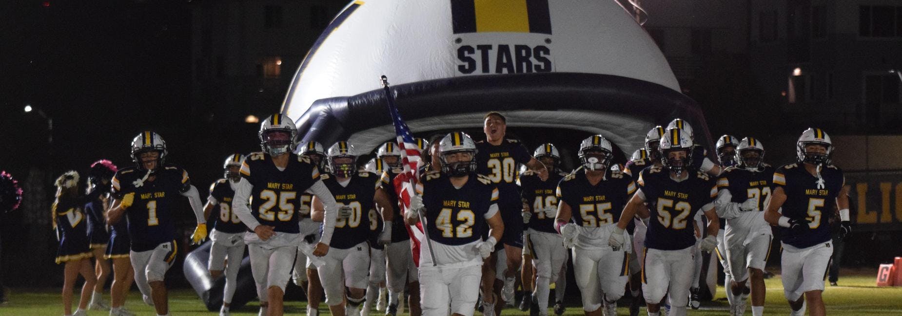 Football team running onto the field from an inflatable helmet tunnel with "STARS"