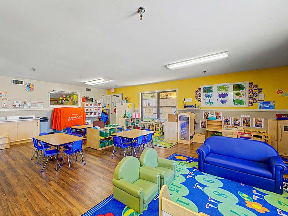 Classroom with small tables and chairs, a blue sofa, and a green rug
