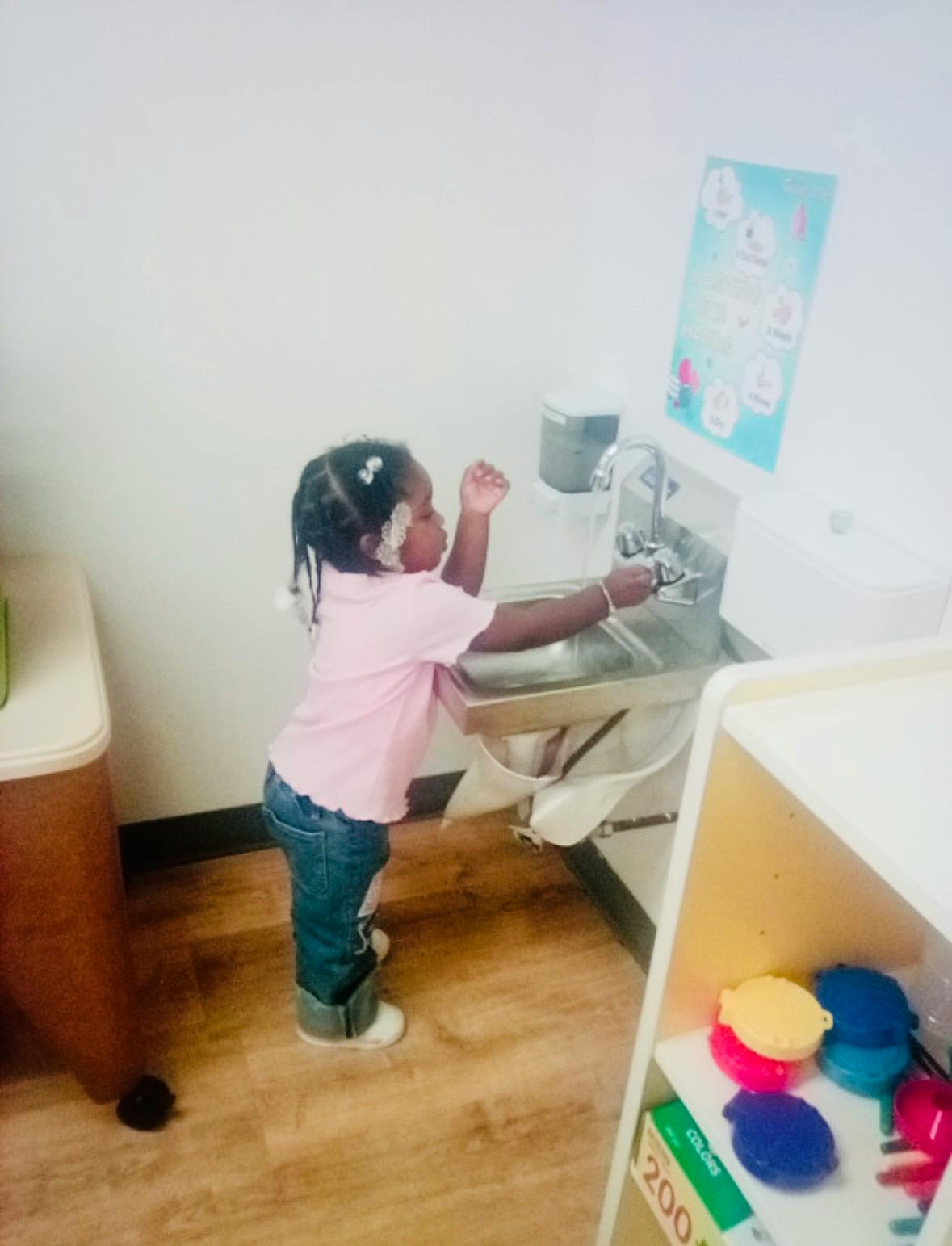 Child standing at a sink, reaching for the faucet