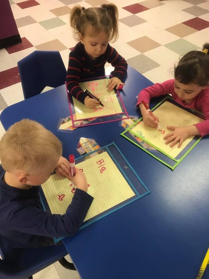 Three children writing on papers at a blue table