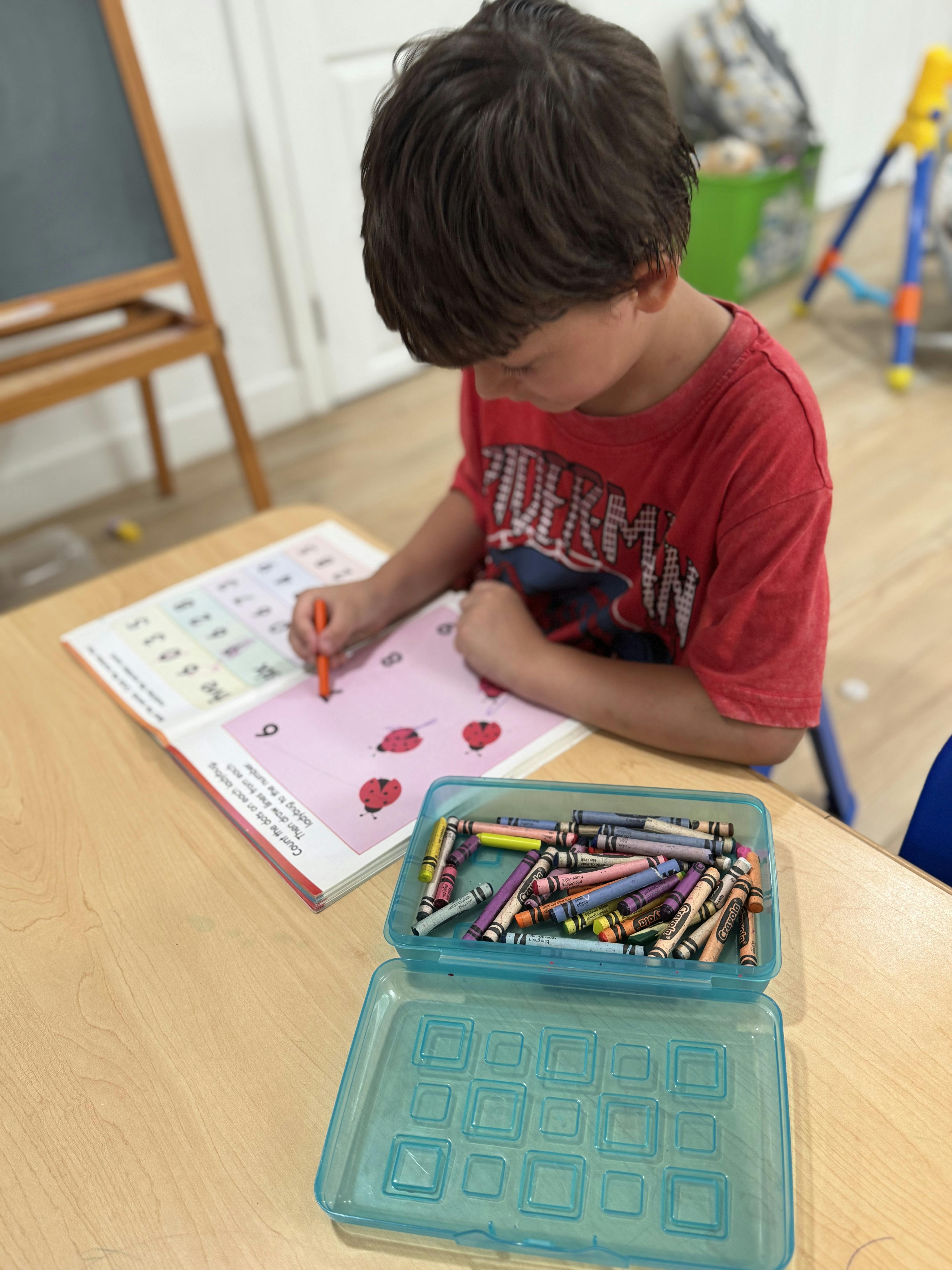 Child coloring in a workbook at a table with crayons