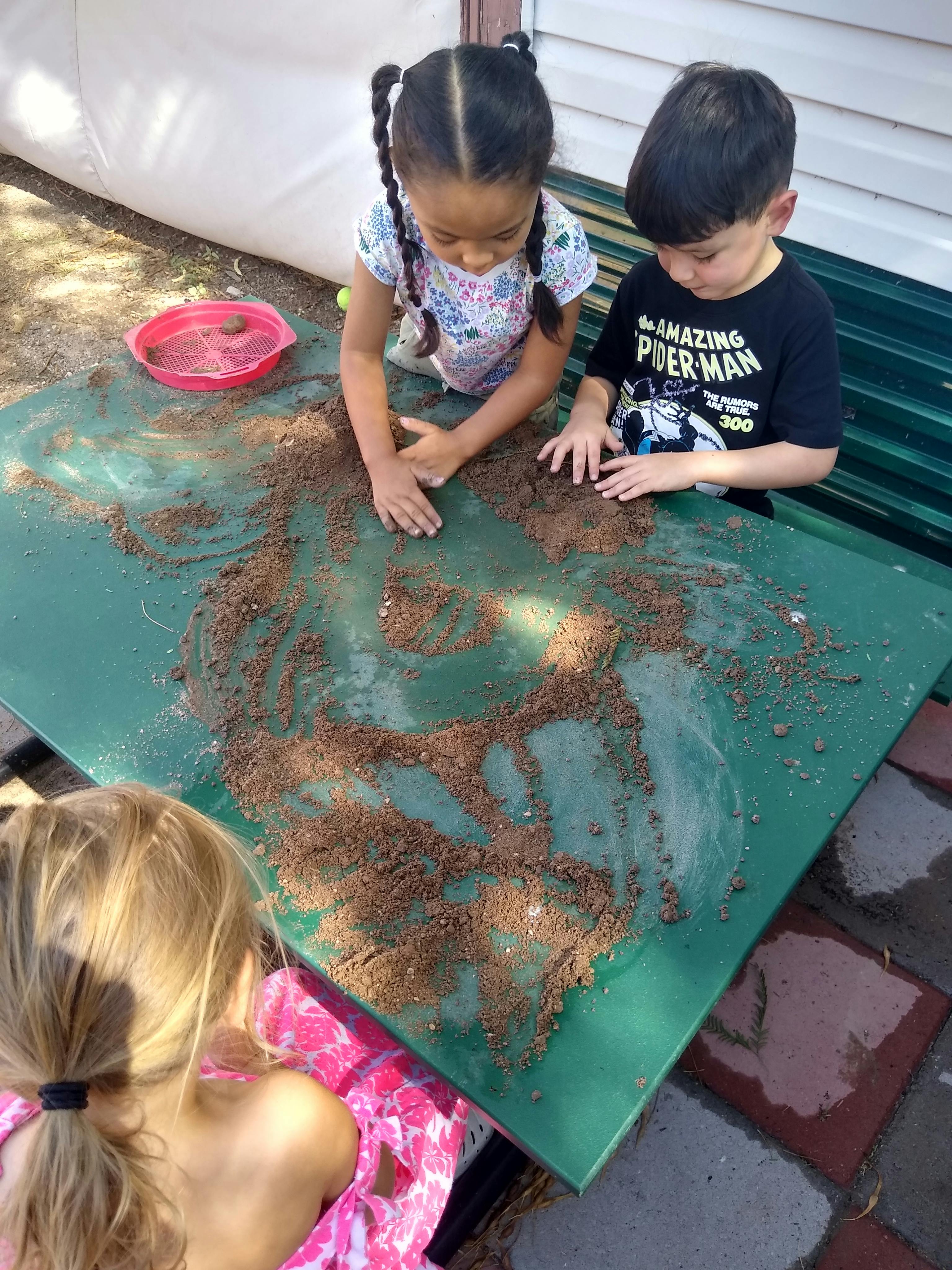 Three children playing with dirt on a plastic table