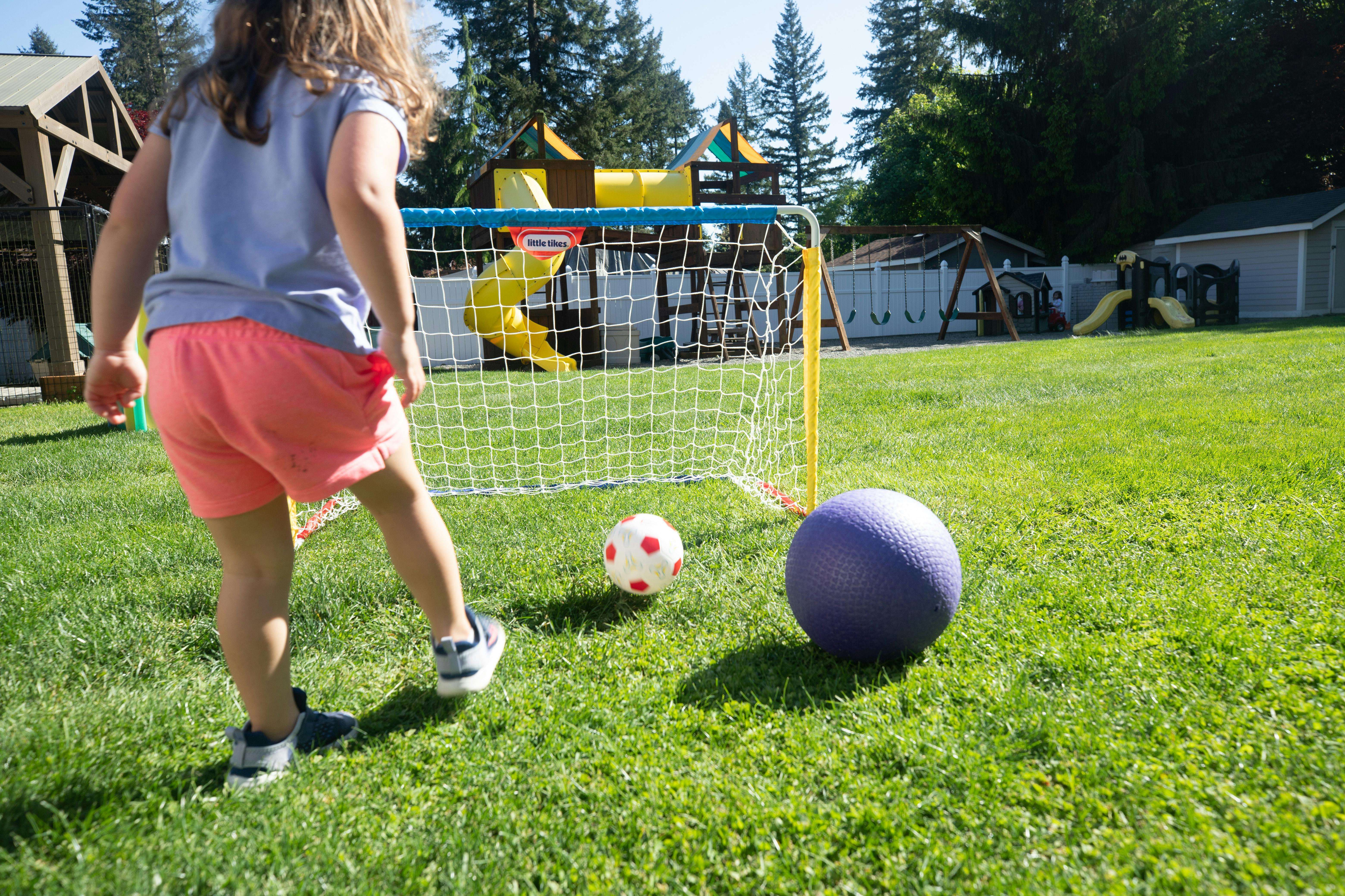 Child kicking a soccer ball towards a small goal in a grassy yard