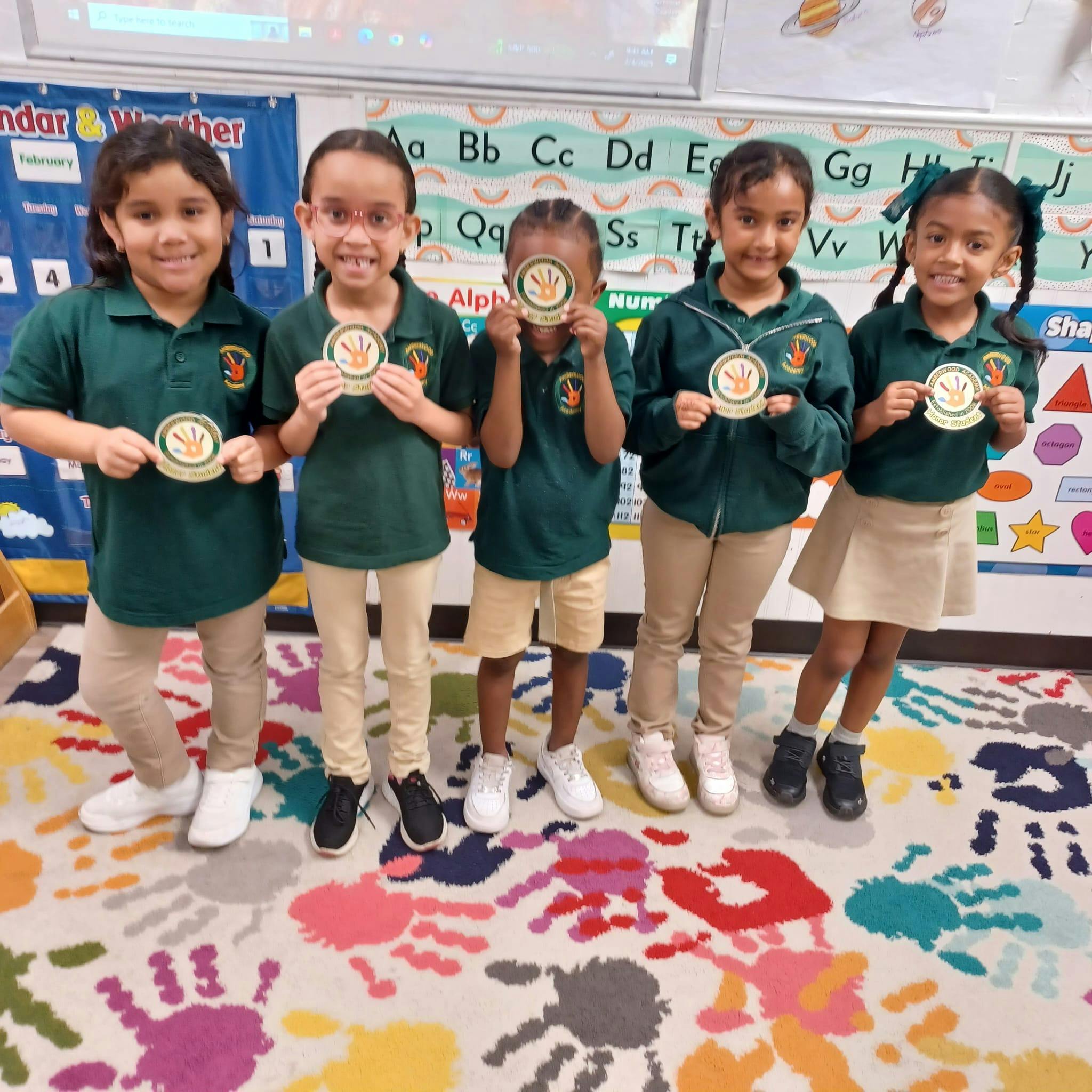 Five children in school uniforms holding up awards in a classroom