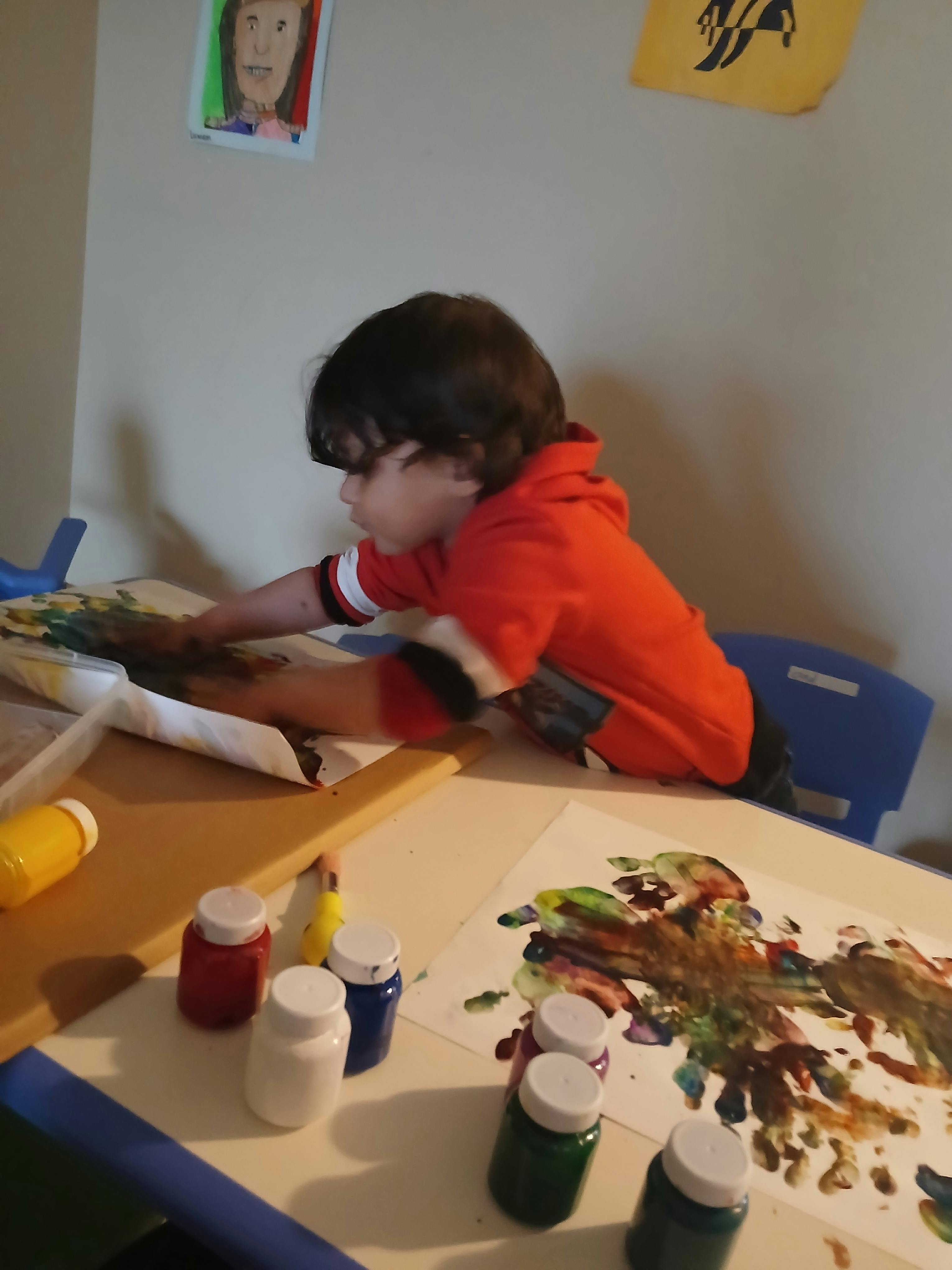 Child finger painting at a table with paint bottles