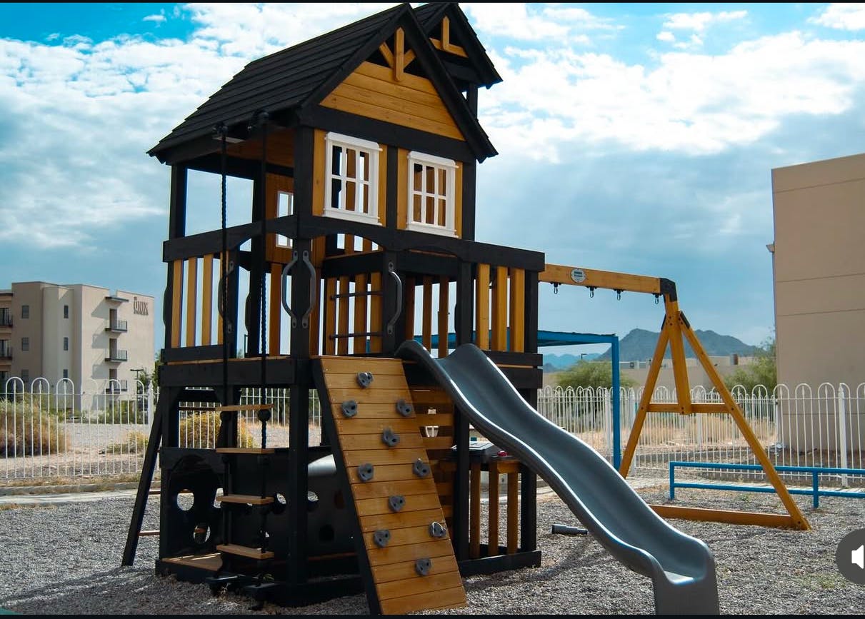 Playground with a wooden playhouse, slide, and swing set