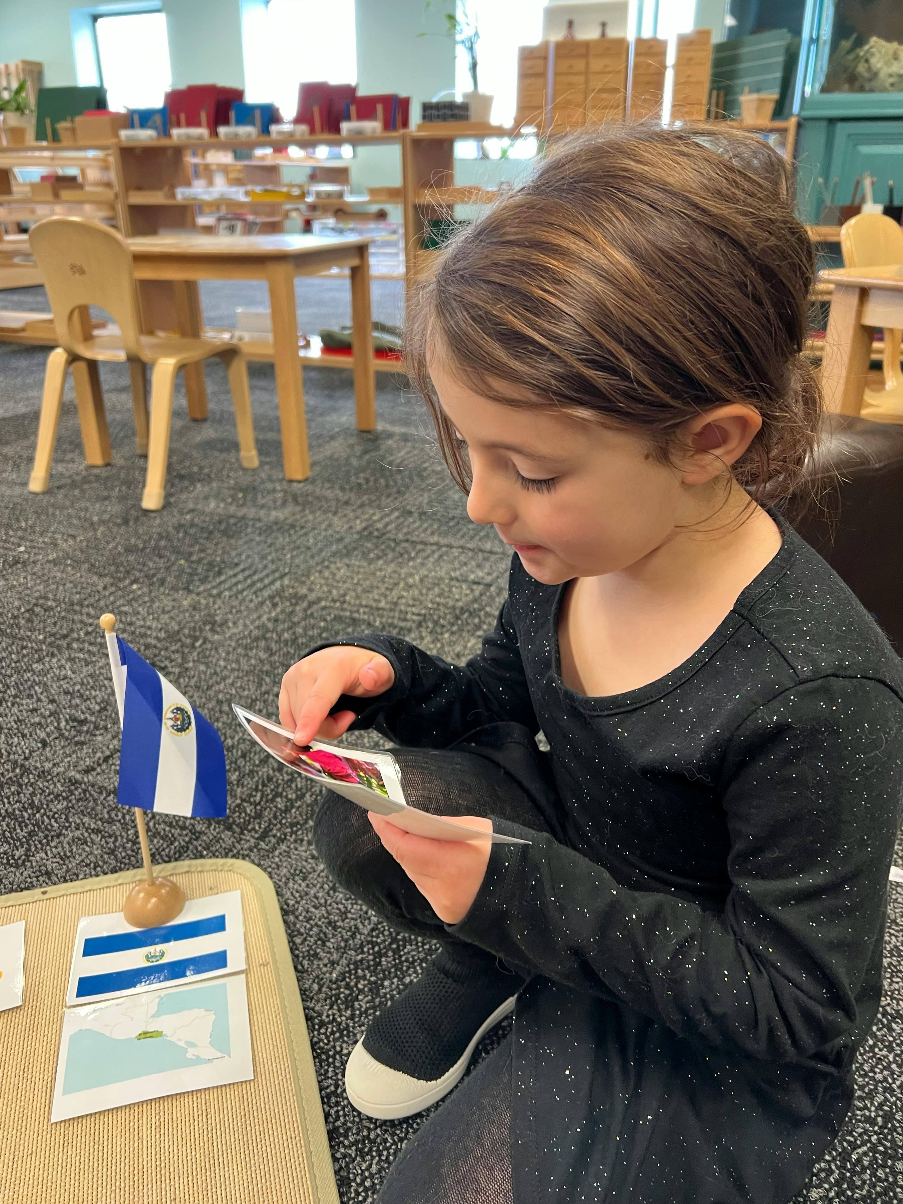 Child looking at cards next to a small flag in a classroom