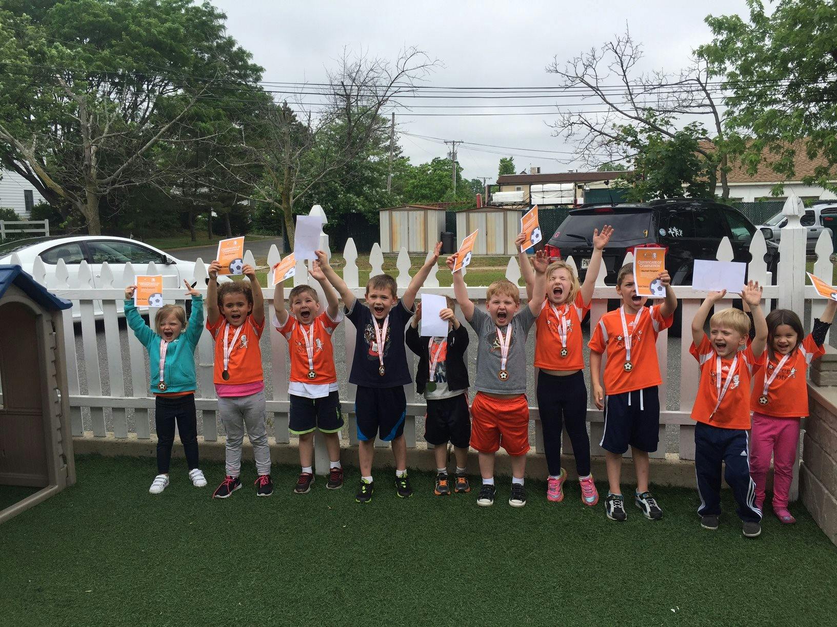 Group of children holding papers and medals with arms raised