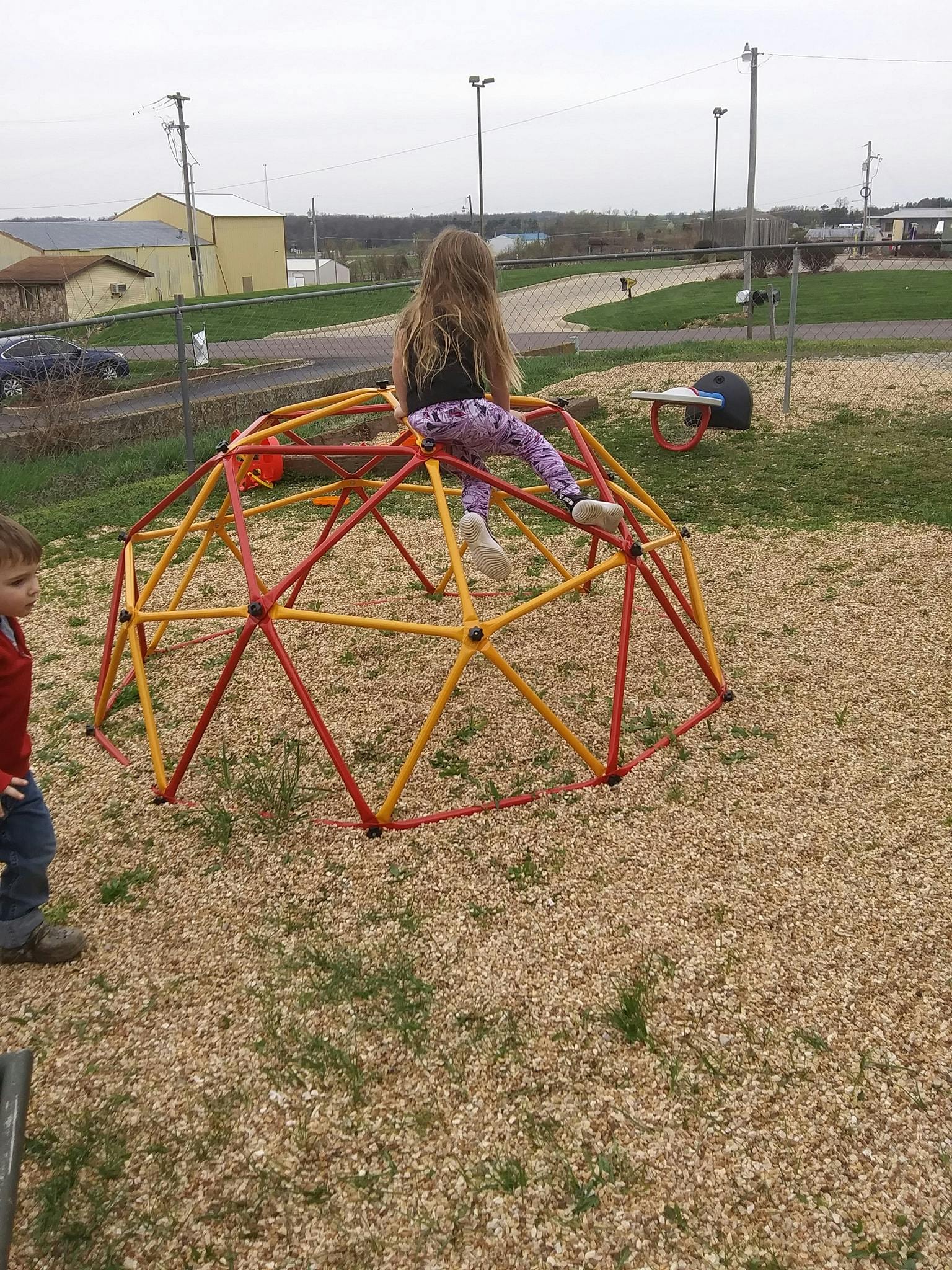 Child climbing on a red and yellow geodesic dome in a playground