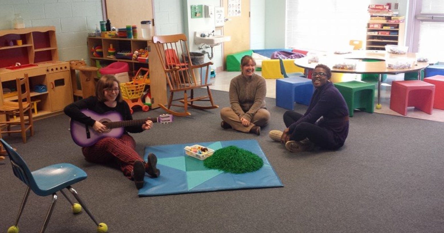 Three people sitting on the floor, one playing a guitar