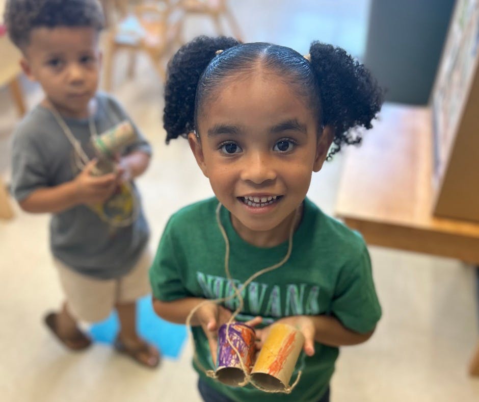 Child holding two decorated cardboard tubes, another child in background