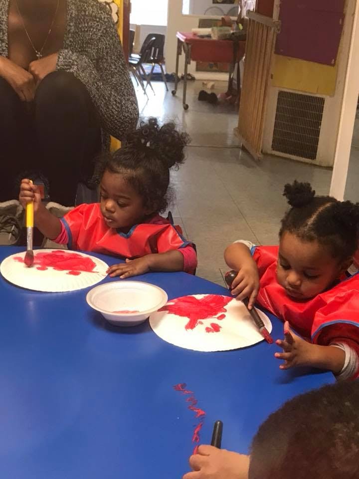 Two children painting with red paint on paper plates at a blue table