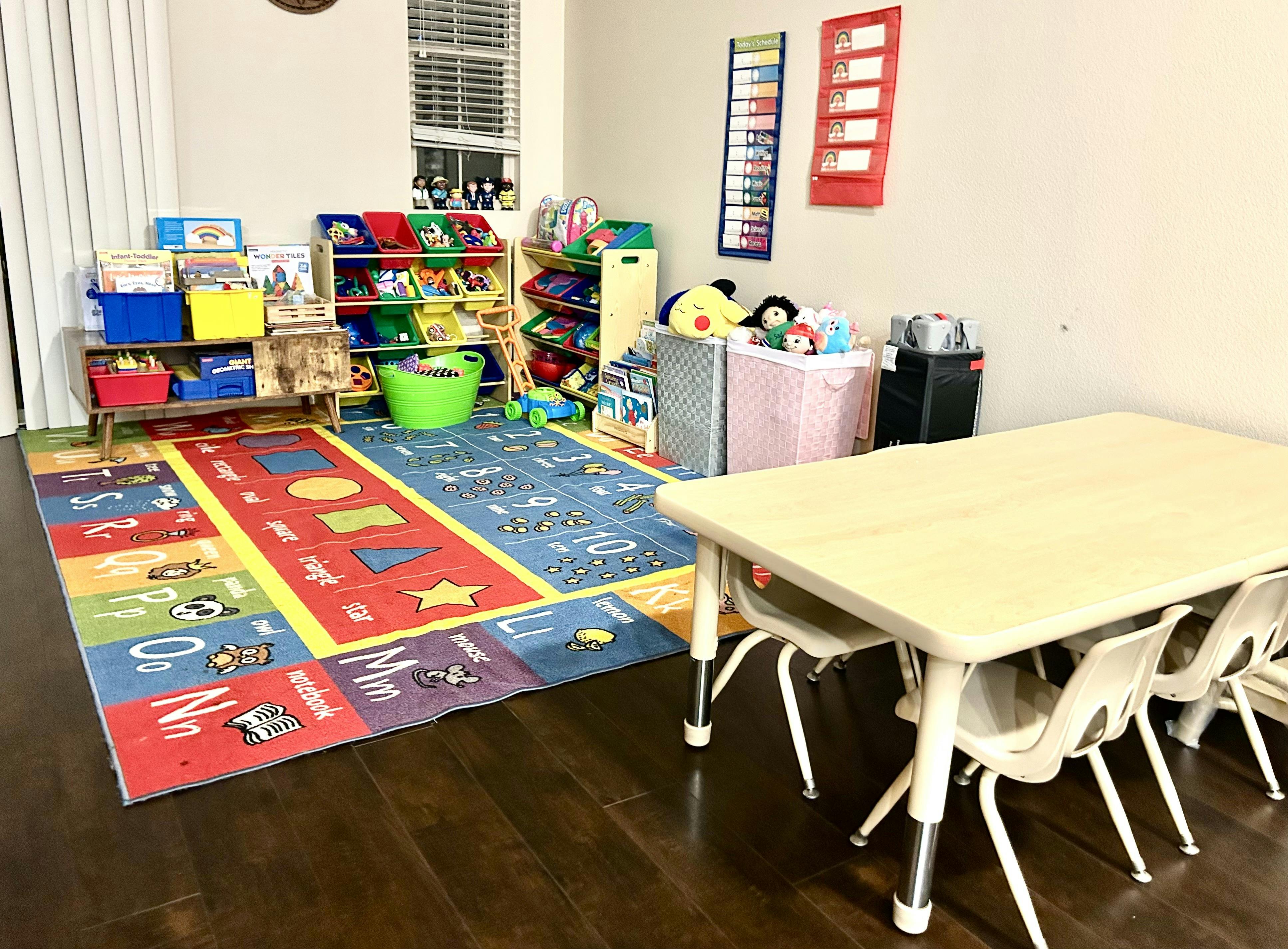 Classroom with a colorful rug, toy shelves, and a table with chairs